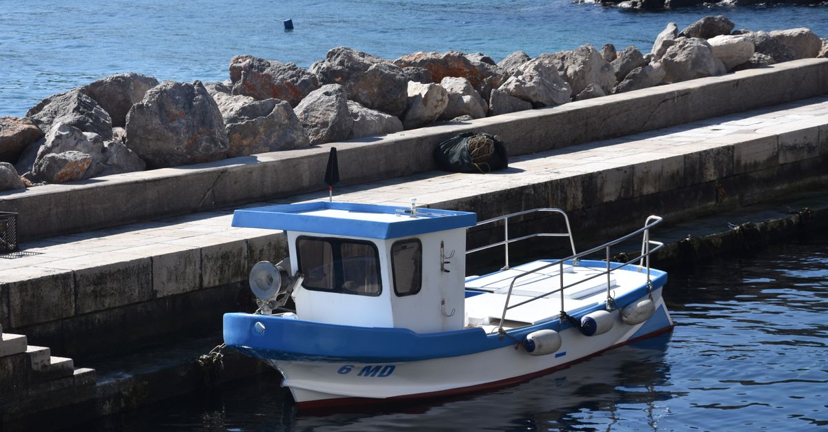 Rampa de pasarela que va desde un muelle de piedra hacia un pequeño barco amarrado