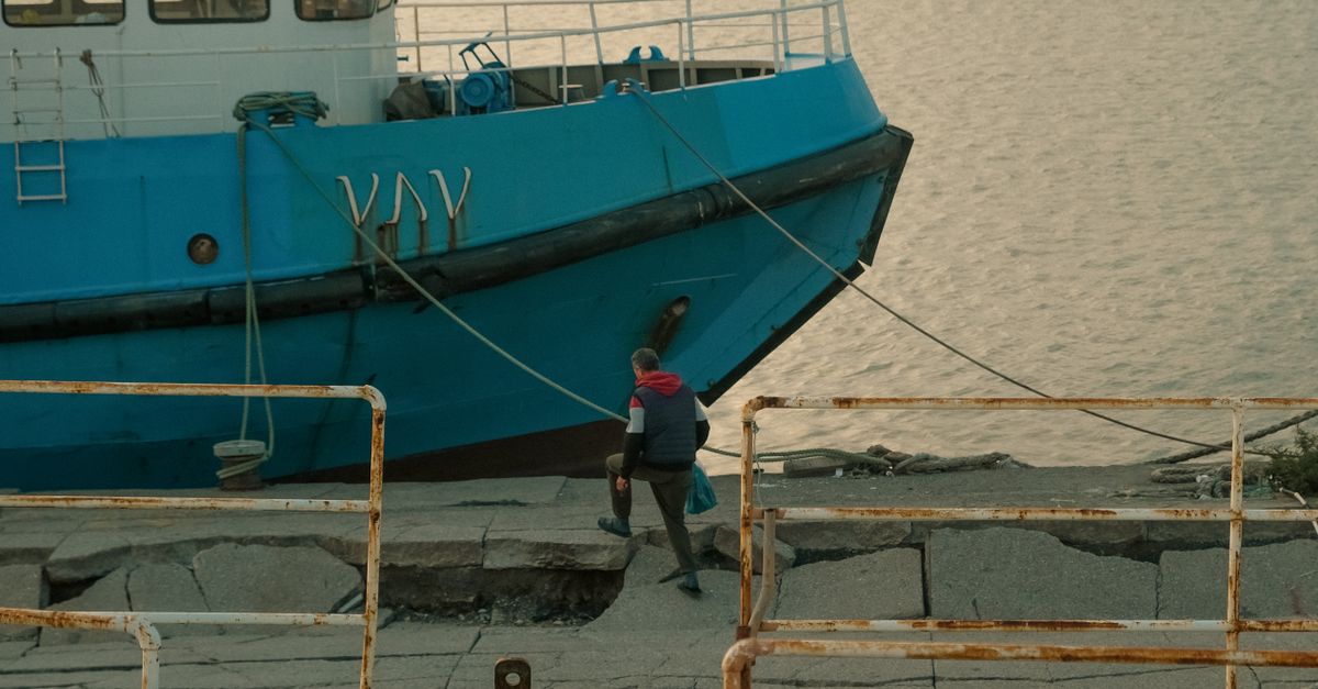 Rampa de pasarela que conduce desde un muelle de piedra hacia un pequeño barco amarrado